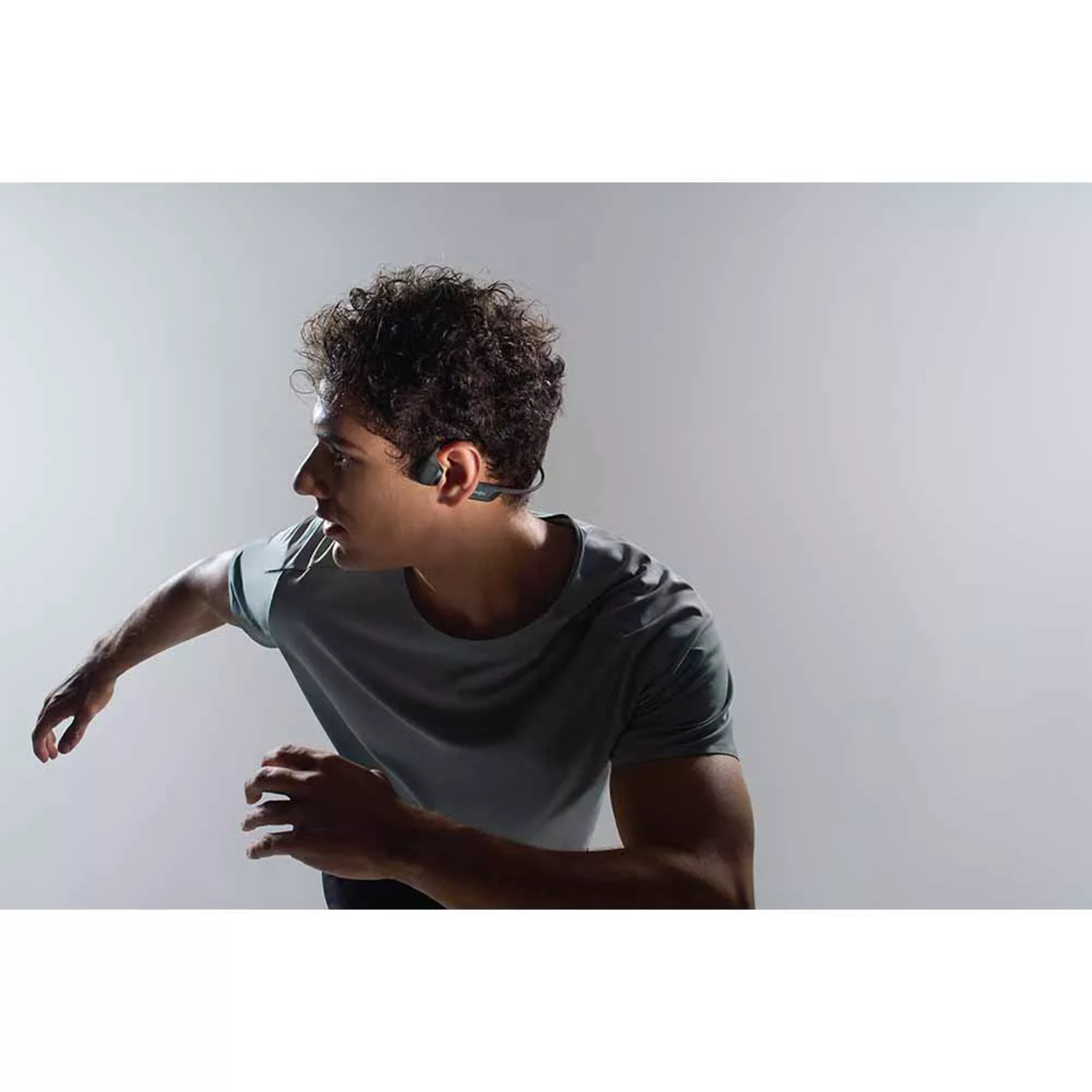 A man running with bone conduction headphones on, set against a gray, gradient background.
