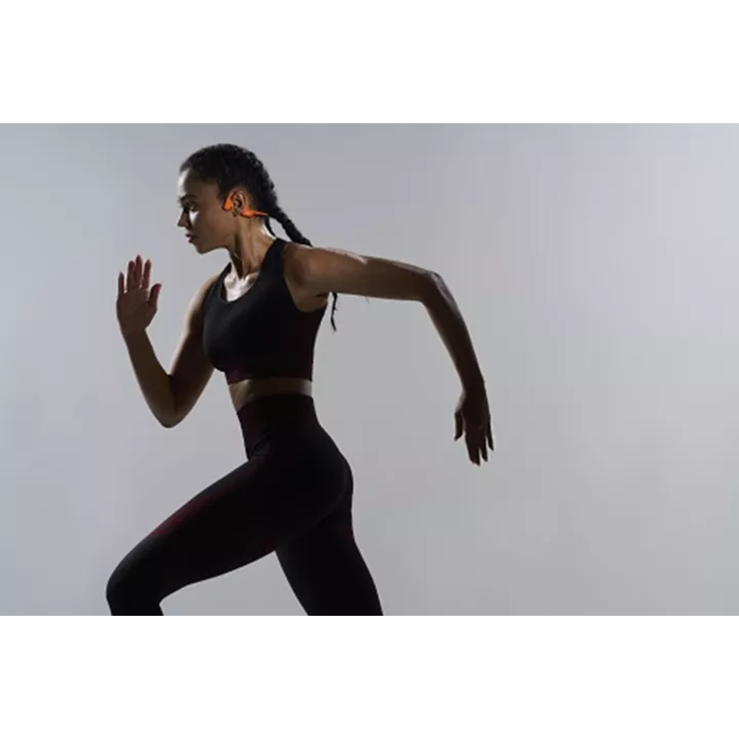A woman running. She wears a black sports bra and leggings, orange headphones.