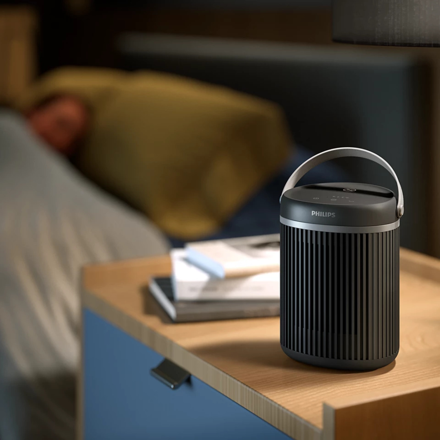 Black Philips air purifier on a nightstand, with a person sleeping in bed.