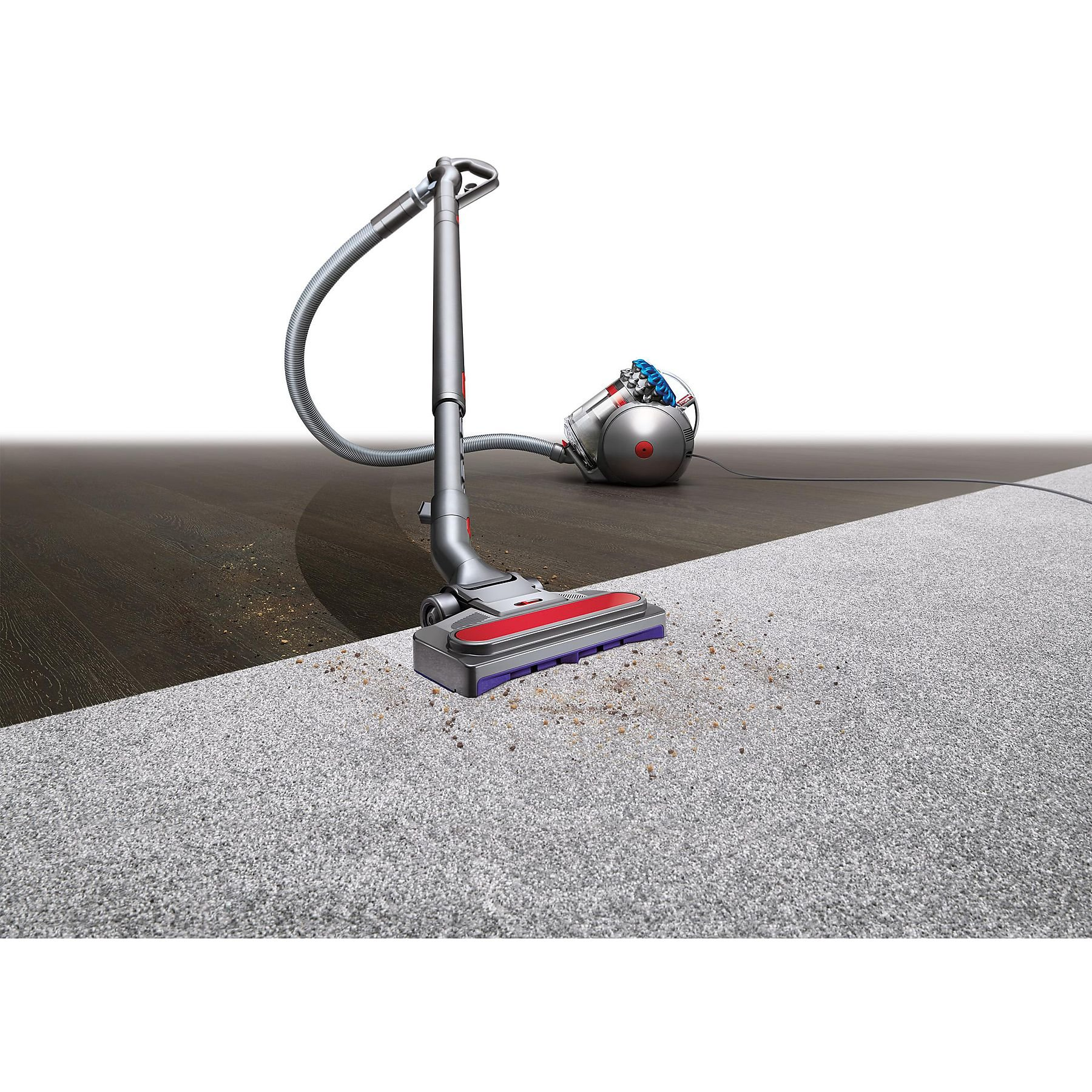 Dyson vacuum cleaner on carpet, cleaning. Dust and debris are visible on the floor.