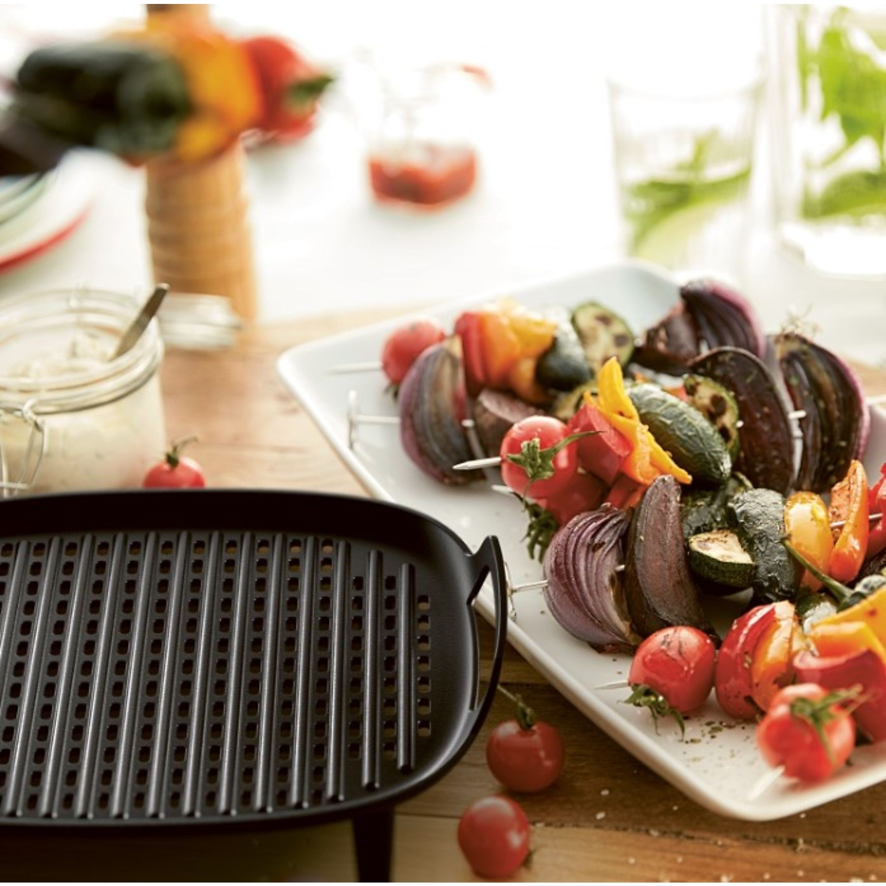Szaszłyki z grillowanymi warzywami na białym talerzu, z czarnym grillem i słoikami.