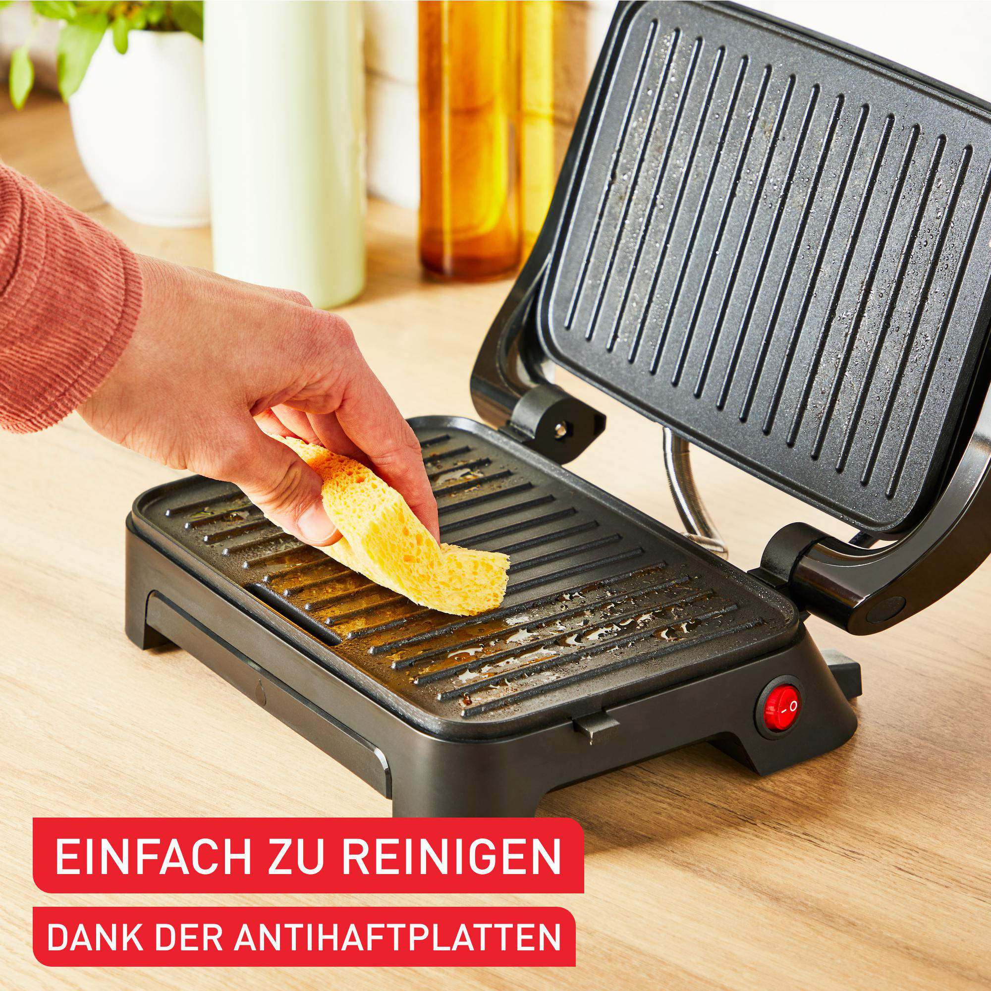 Hand legt Brot auf offenen Grill. Roter Einschaltknopf sichtbar.