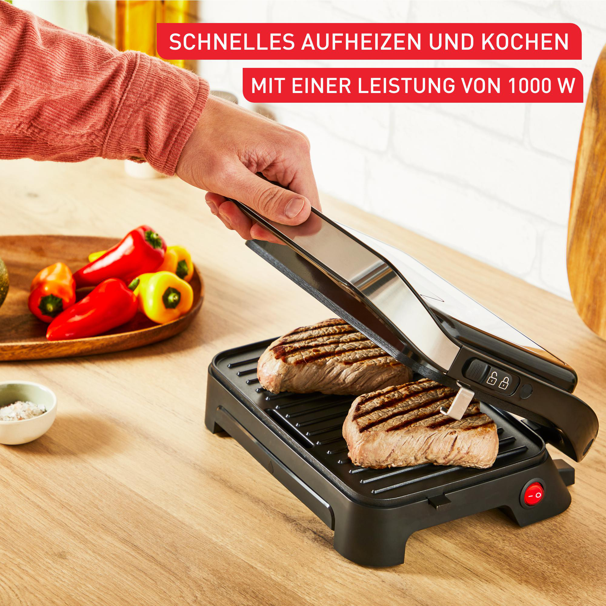 Person grillt Steaks auf einem schwarzen Grill mit roten und gelben Paprika daneben.