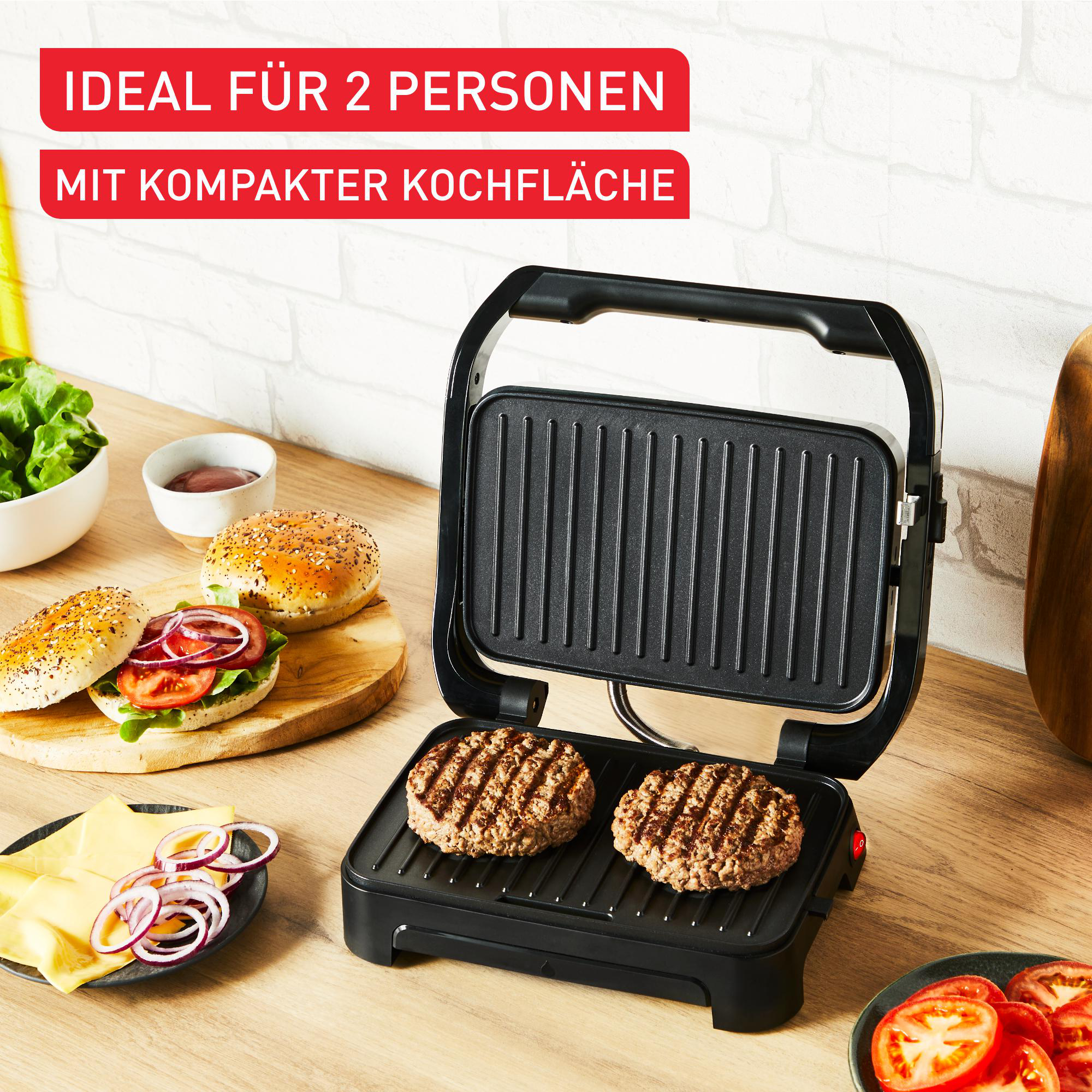 Offener schwarzer Indoor-Grill mit zwei bratenburgern, Brötchen und Zutaten in der Nähe. Holzoberfläche.