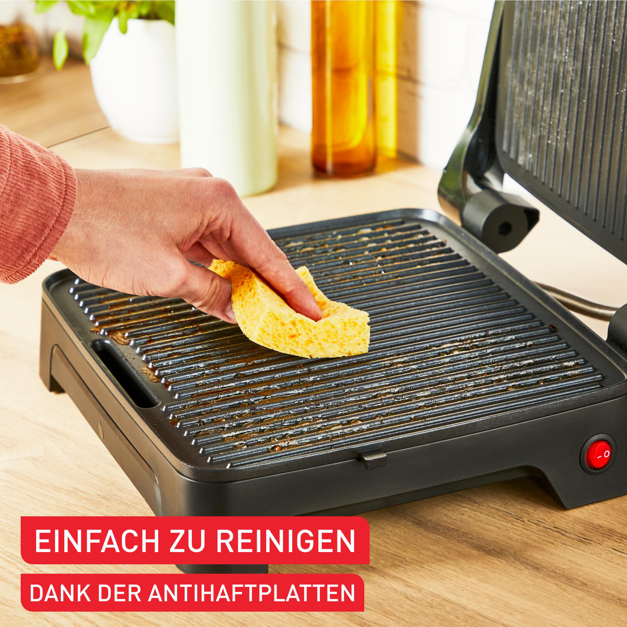Hand reinigt schwarzen Grill mit gelbem Schwamm. Text: 'Einfach zu reinigen' und 'Dank der Antihaftplatten'.