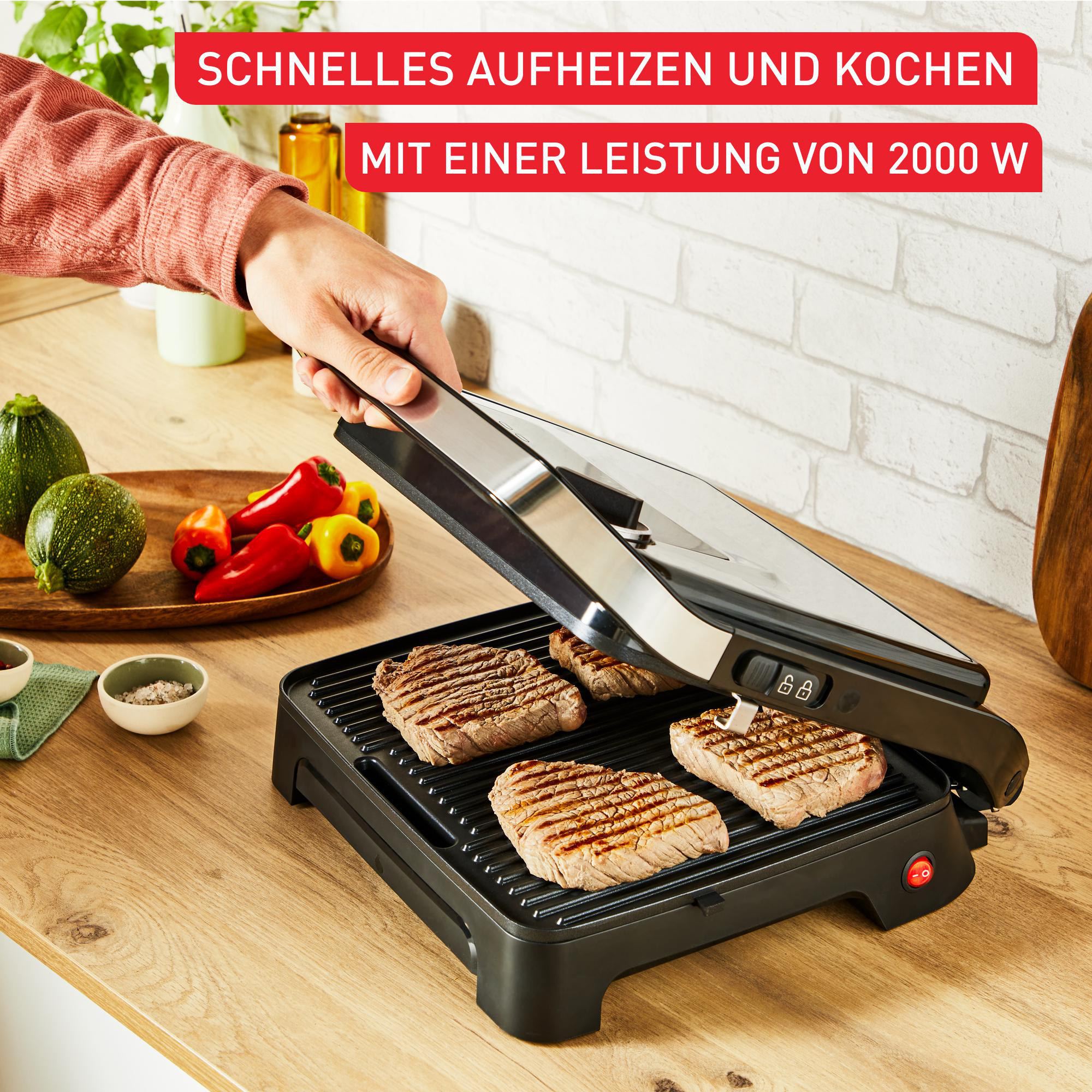 Eine Person öffnet einen Grill mit bratenen Steaks. Gemüse und Gewürze stehen auf der Holztheke neben dem Grill.