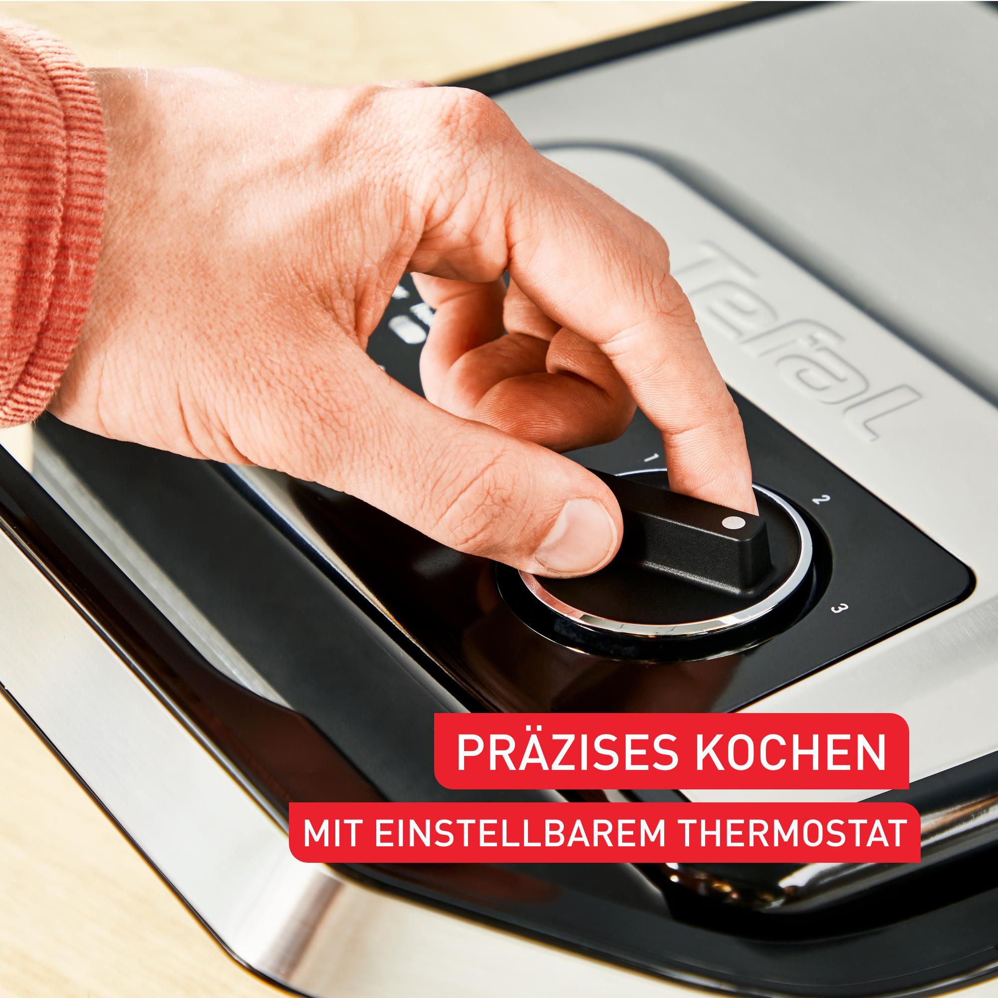 Eine Hand dreht einen schwarzen Knopf an einem silber-schwarzen Gerät. Text: Präzises Kochen.