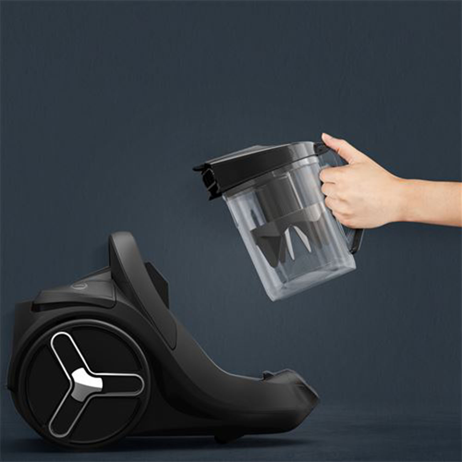 Un aspirapolvere nero e un contenitore di plastica trasparente tenuto in mano.