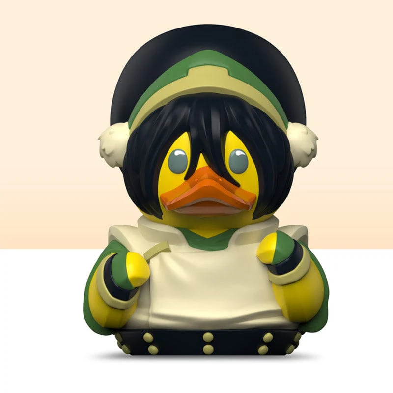 Toph Avatar karakter gumikacsa játék. Sárga test, fekete haj és zöld ruhák. Fehér háttér.