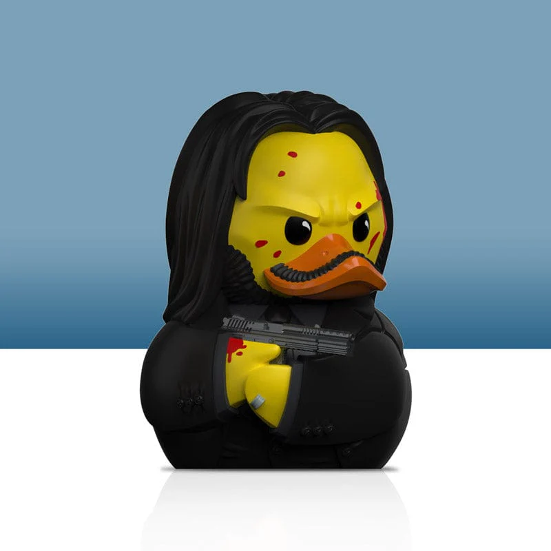 Gumikacsa John Wick arcával, fegyvert tartva. Vérfoltok az arcon.