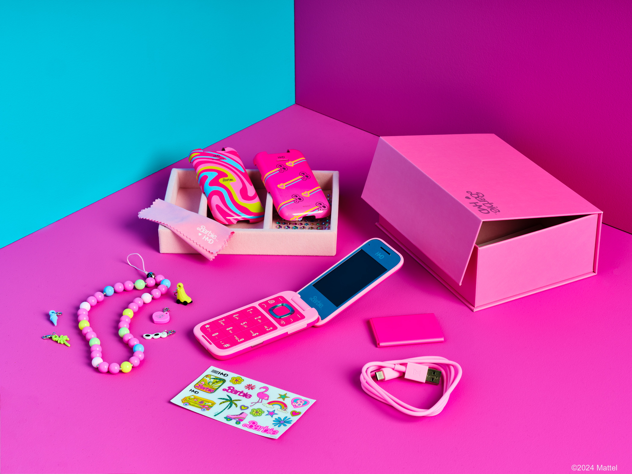 Egy Barbie kagylótelefon kiegészítőkkel, beleértve egy rózsaszín dobozt, nyakláncot, matricákat és egy USB kábelt.