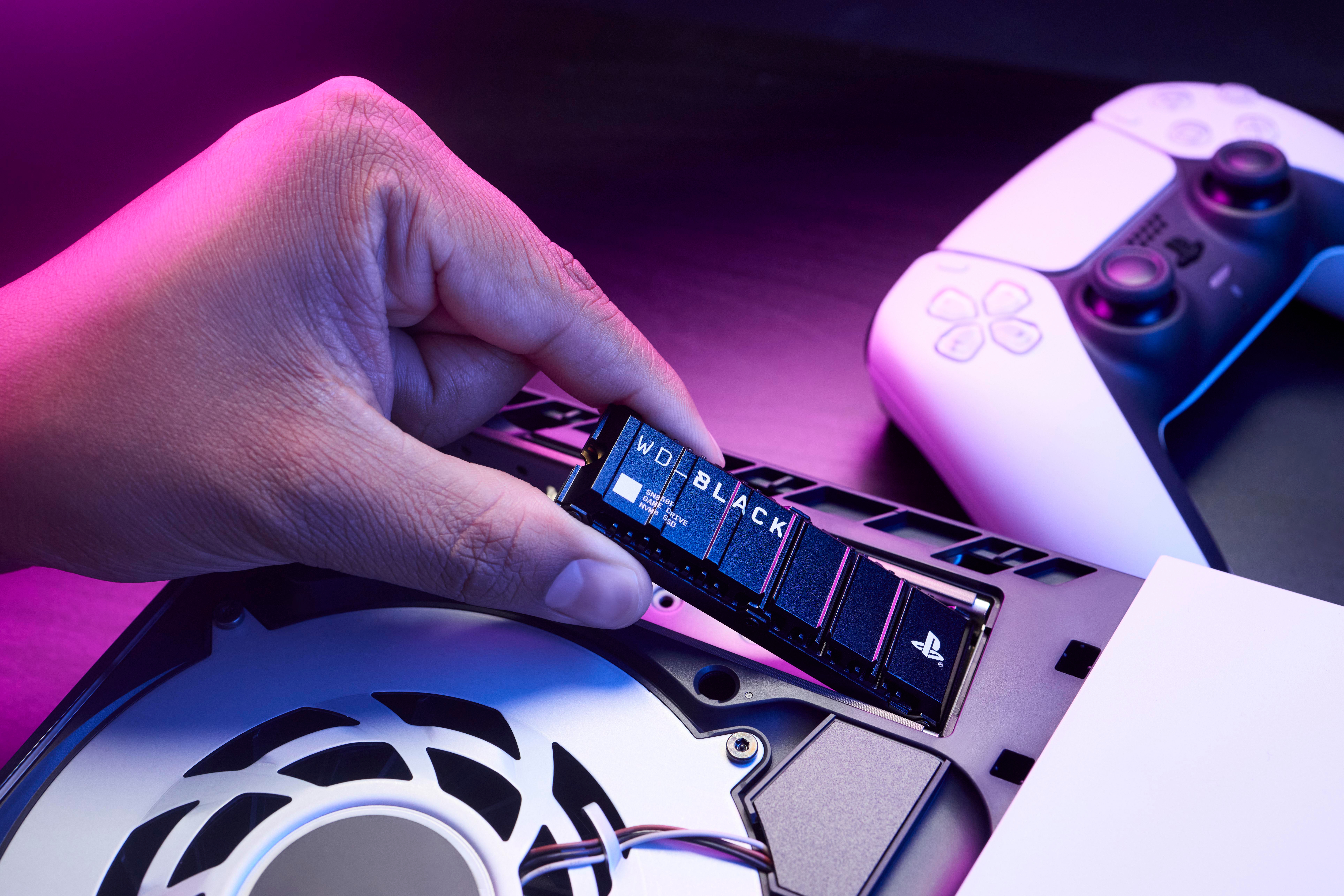 Person setzt eine WD_BLACK SSD in eine PS5 ein. PS5 ist geöffnet. Hand hält die SSD. Dunkler Hintergrund.