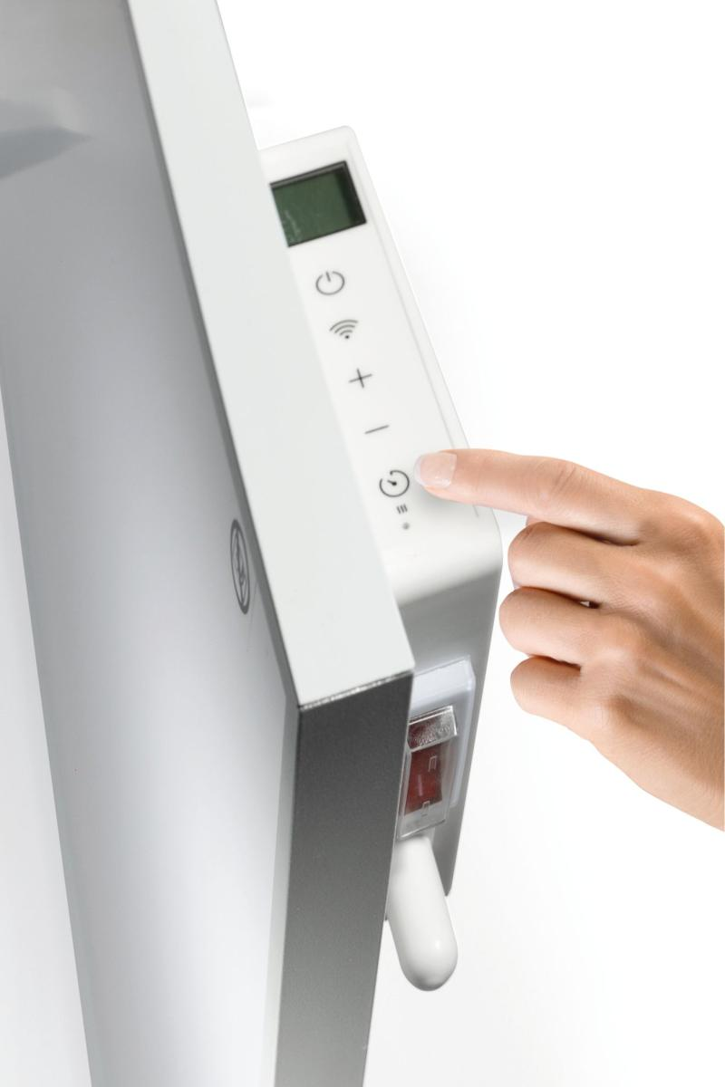 Egy személy keze egy fehér elektromos fűtőtest vezérlőpaneljét érinti.
