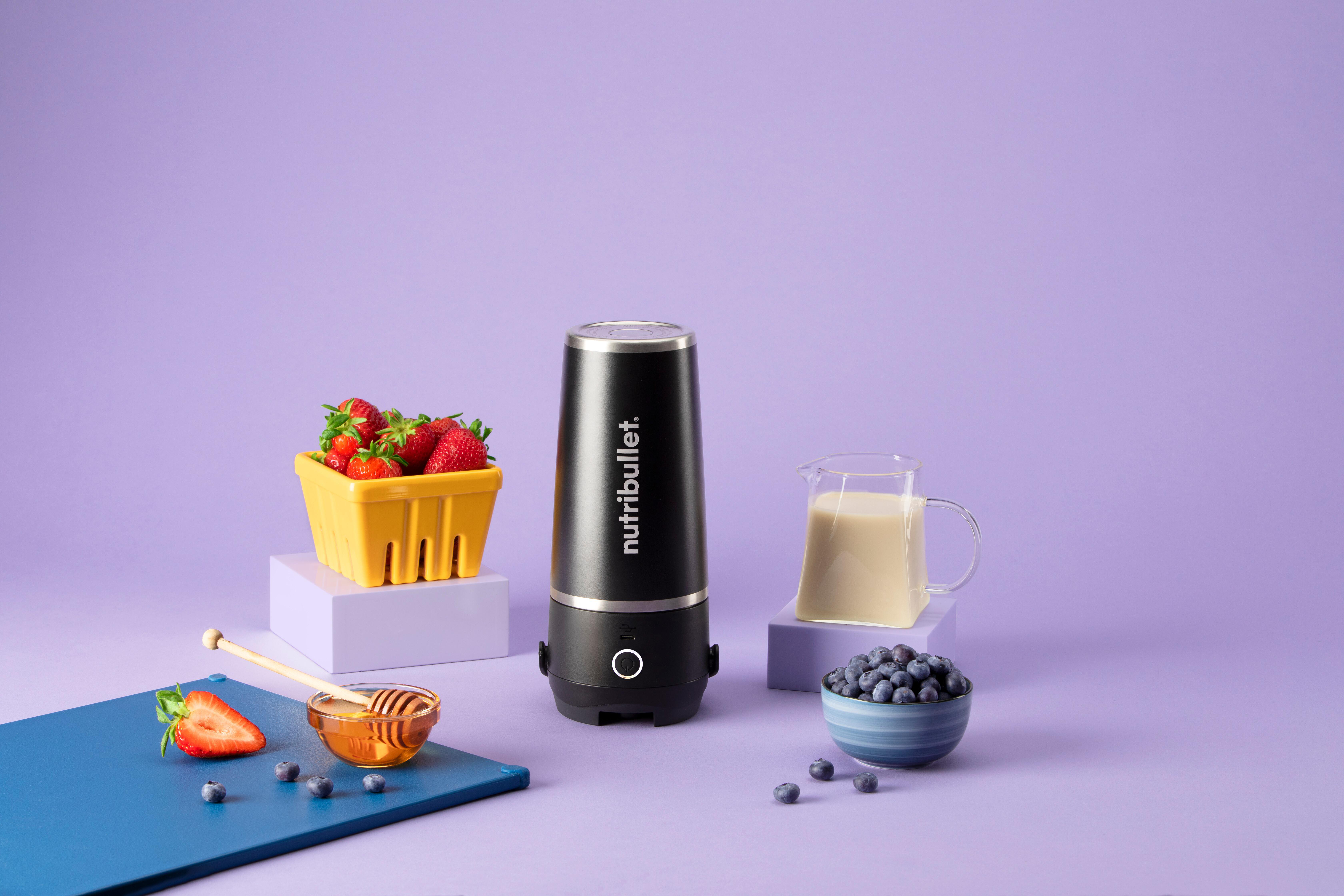 Schwarzer Mixer, Erdbeeren, Blaubeeren, Honig und Milch auf lila Oberfläche.