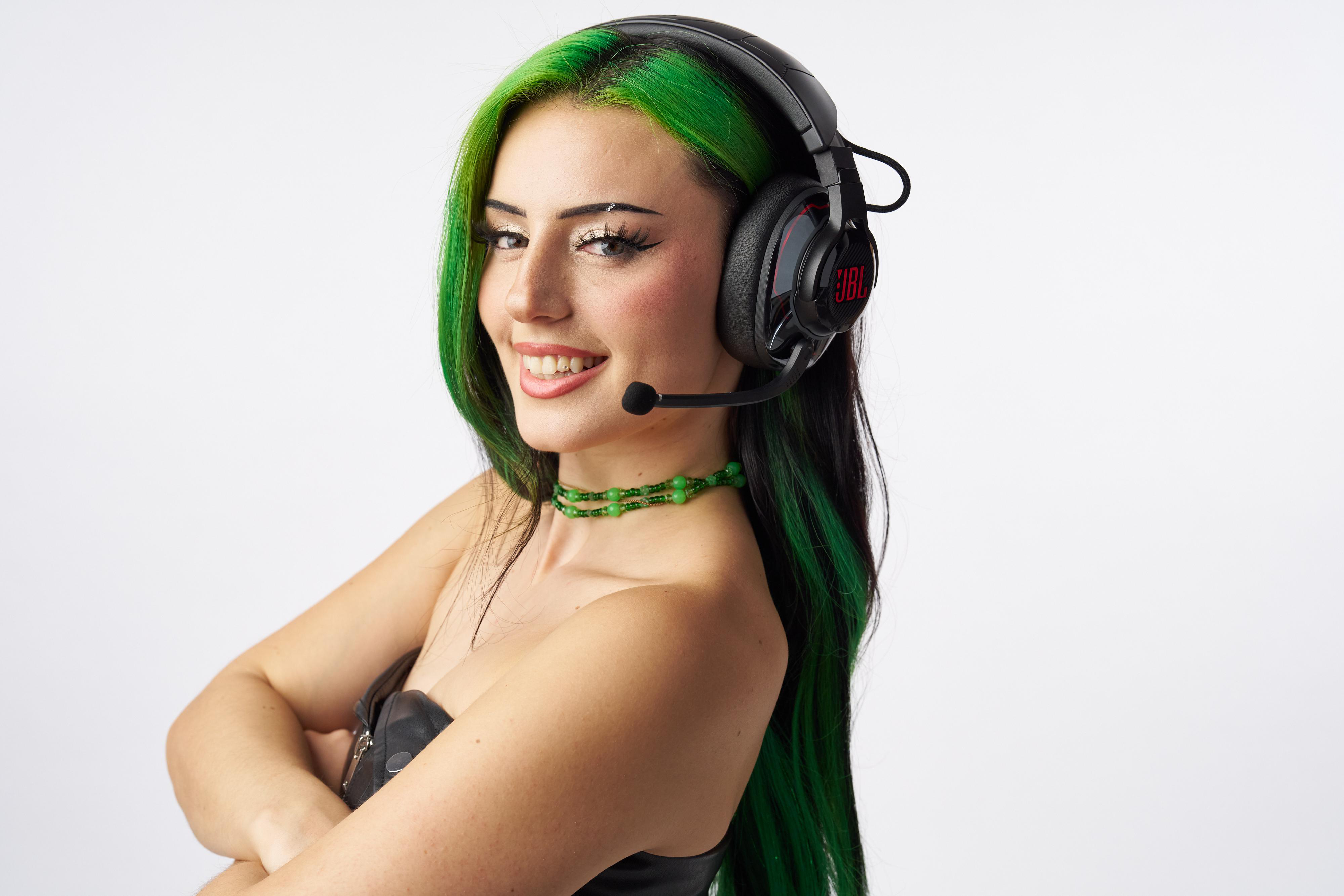 Eine Frau mit grünen Haaren und Headset, lächelnd und zur Seite blickend.