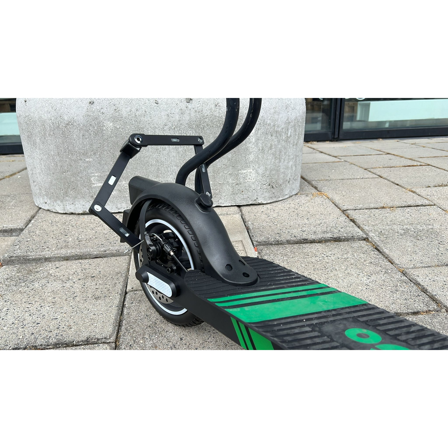 Gros plan de la roue arrière d'une trottinette, garde-boue noir, et plateforme à rayures vertes.