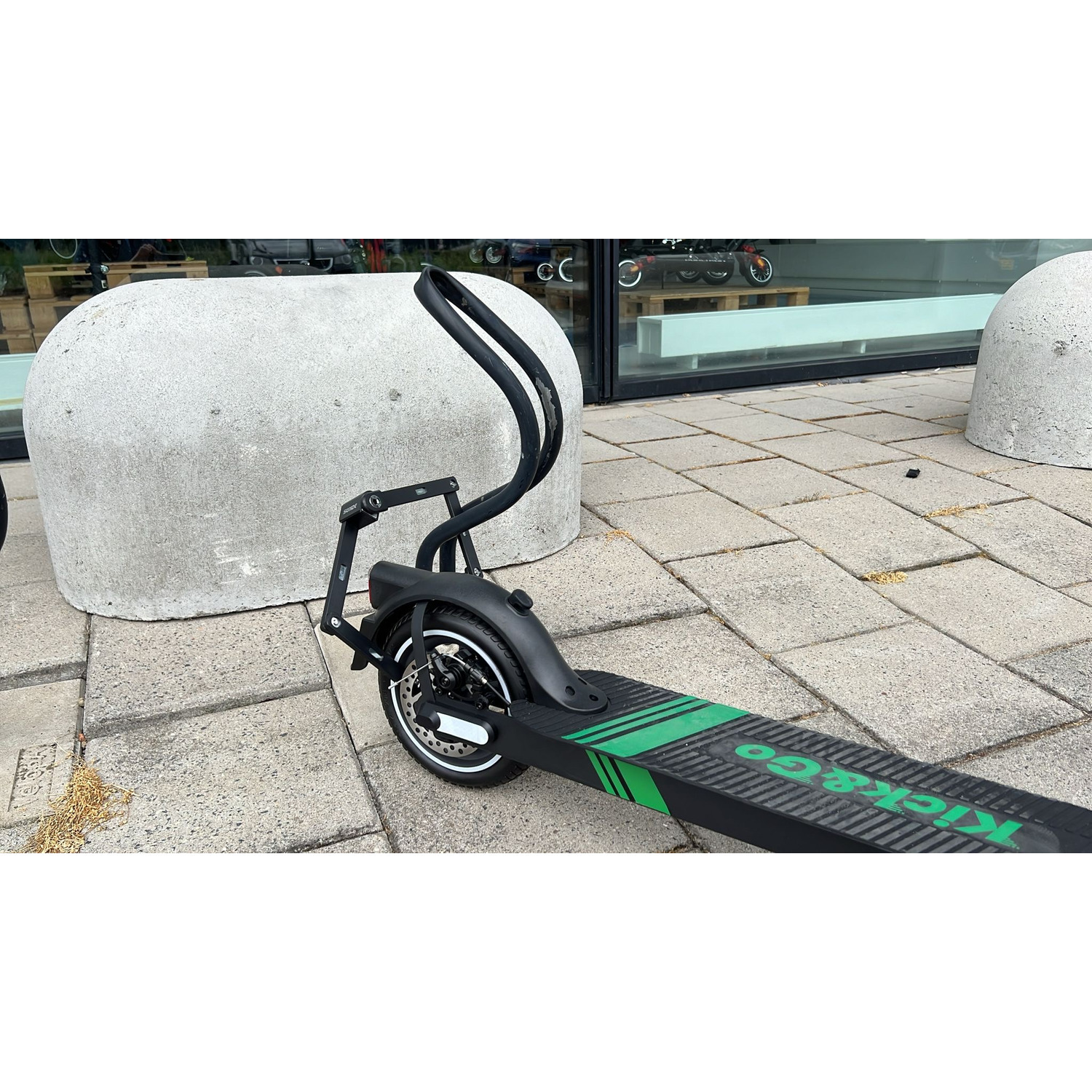 Trottinette électrique noire et verte sur une surface pavée à côté d'un grand objet en béton gris.