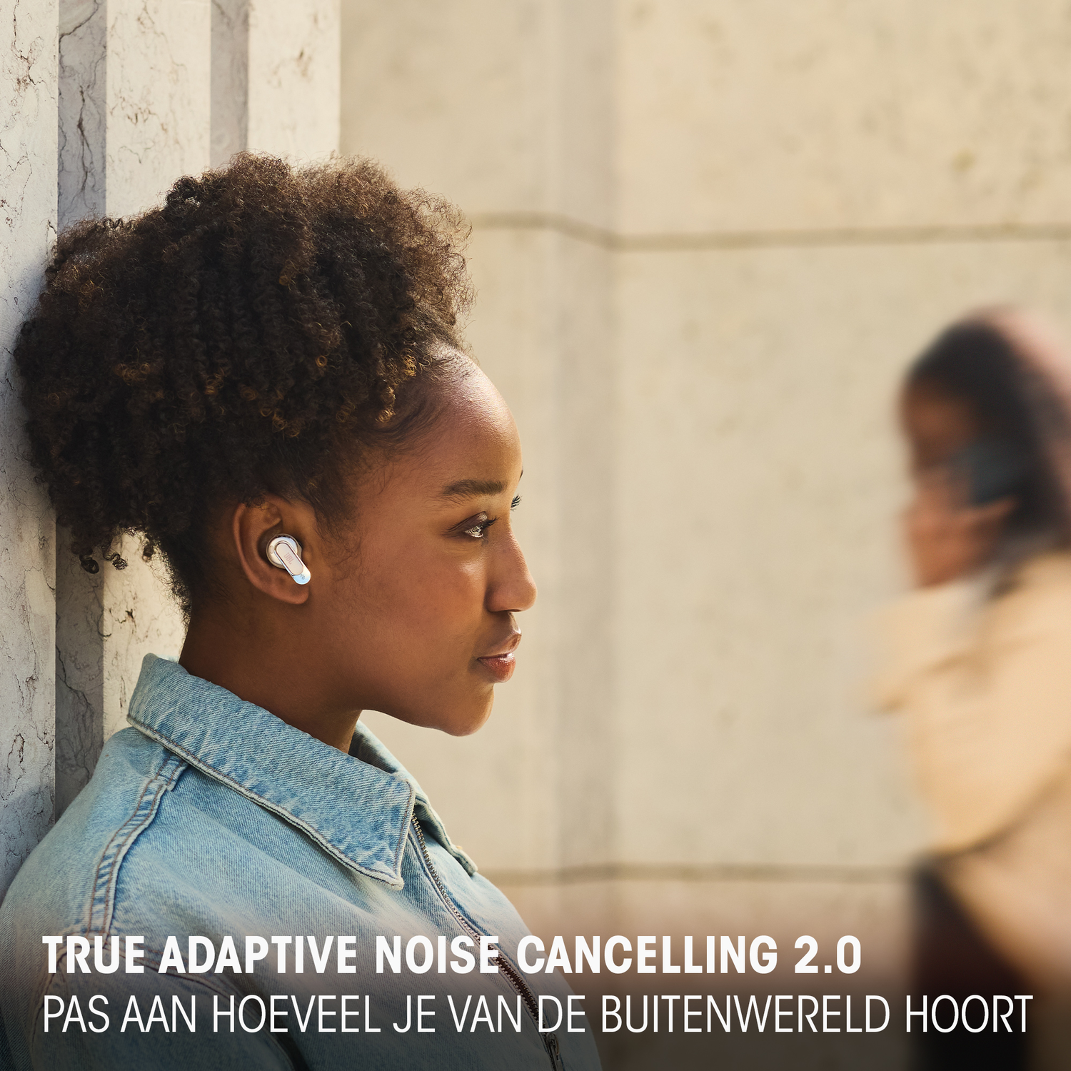 A woman wearing white earbuds with text: True Adaptive Noise Cancelling 2.0. Out of focus background.