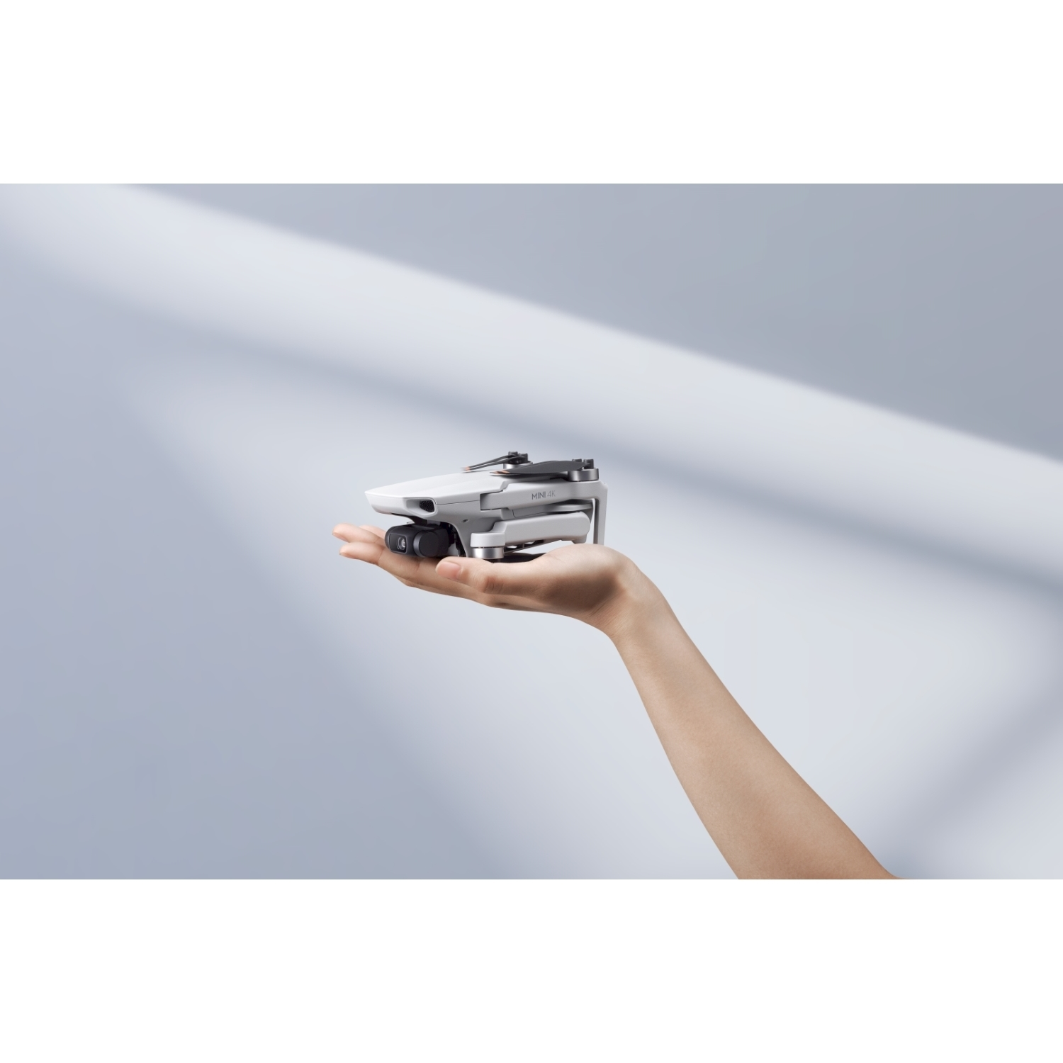 Un drone bianco è tenuto in mano su uno sfondo azzurro.