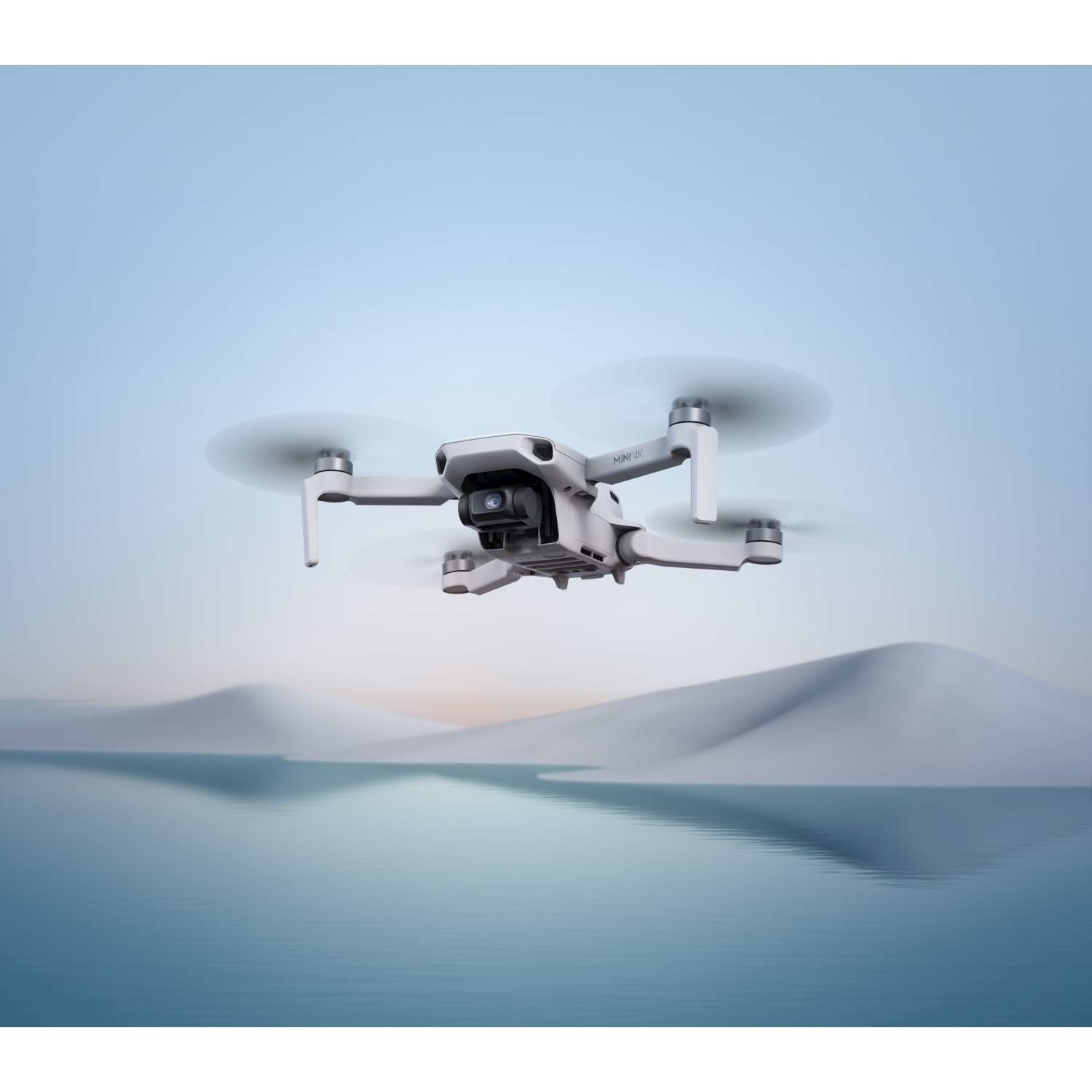 Un drone bianco con quattro eliche vola sopra un lago calmo con montagne sullo sfondo.
