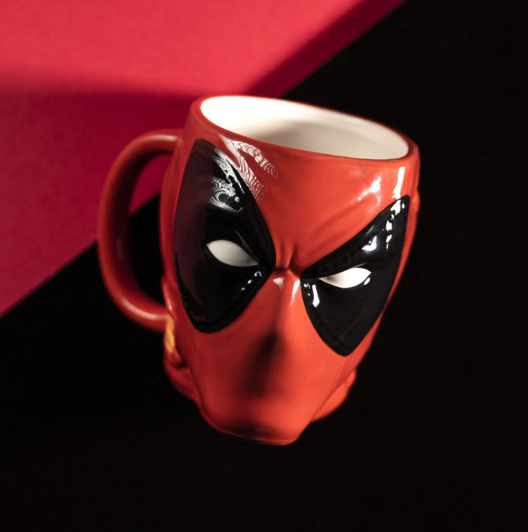 Eine rote Deadpool-Tasse mit schwarzen Augen und einem Griff, auf schwarzem und rotem Untergrund.