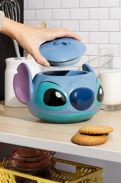 Eine Hand öffnet einen Stitch-Becher. Der Becher ist blau, hat große Ohren und große Augen.