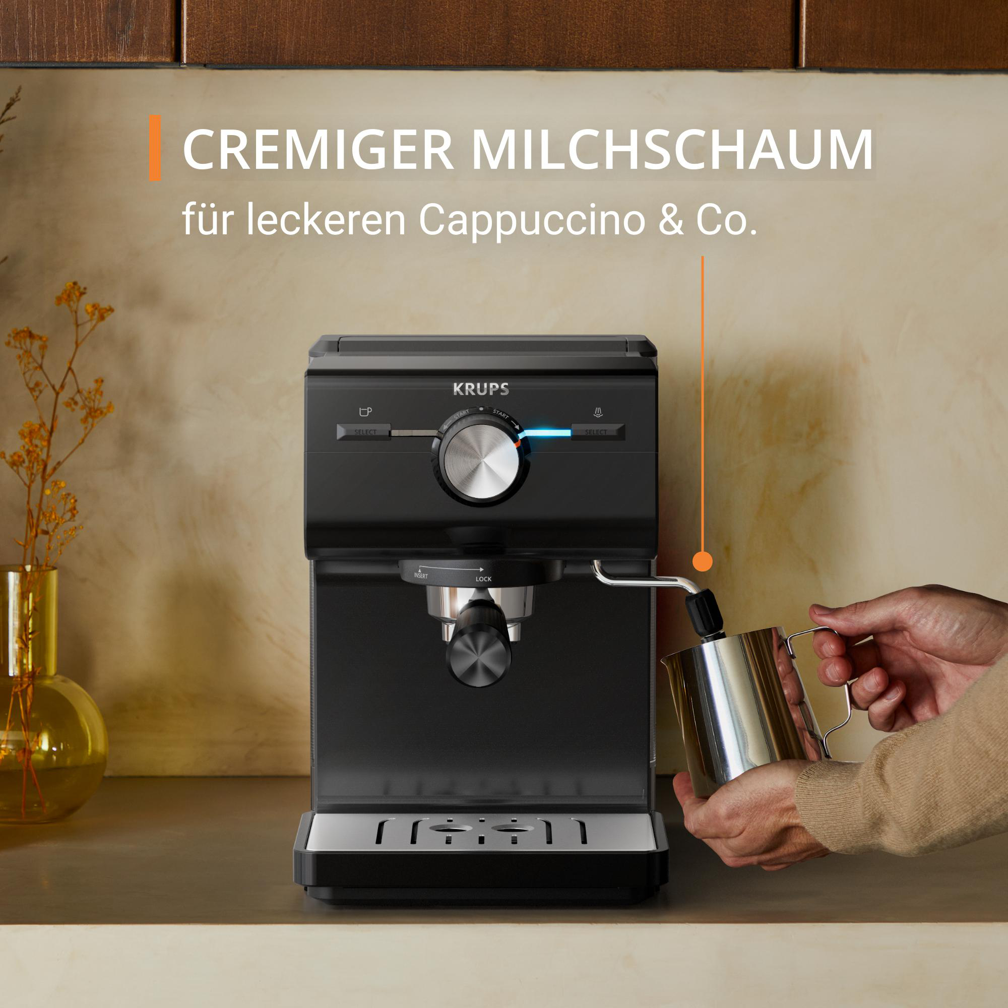 Schwarze Krups Espressomaschine mit einer Hand, die einen Milchaufschäumer hält.