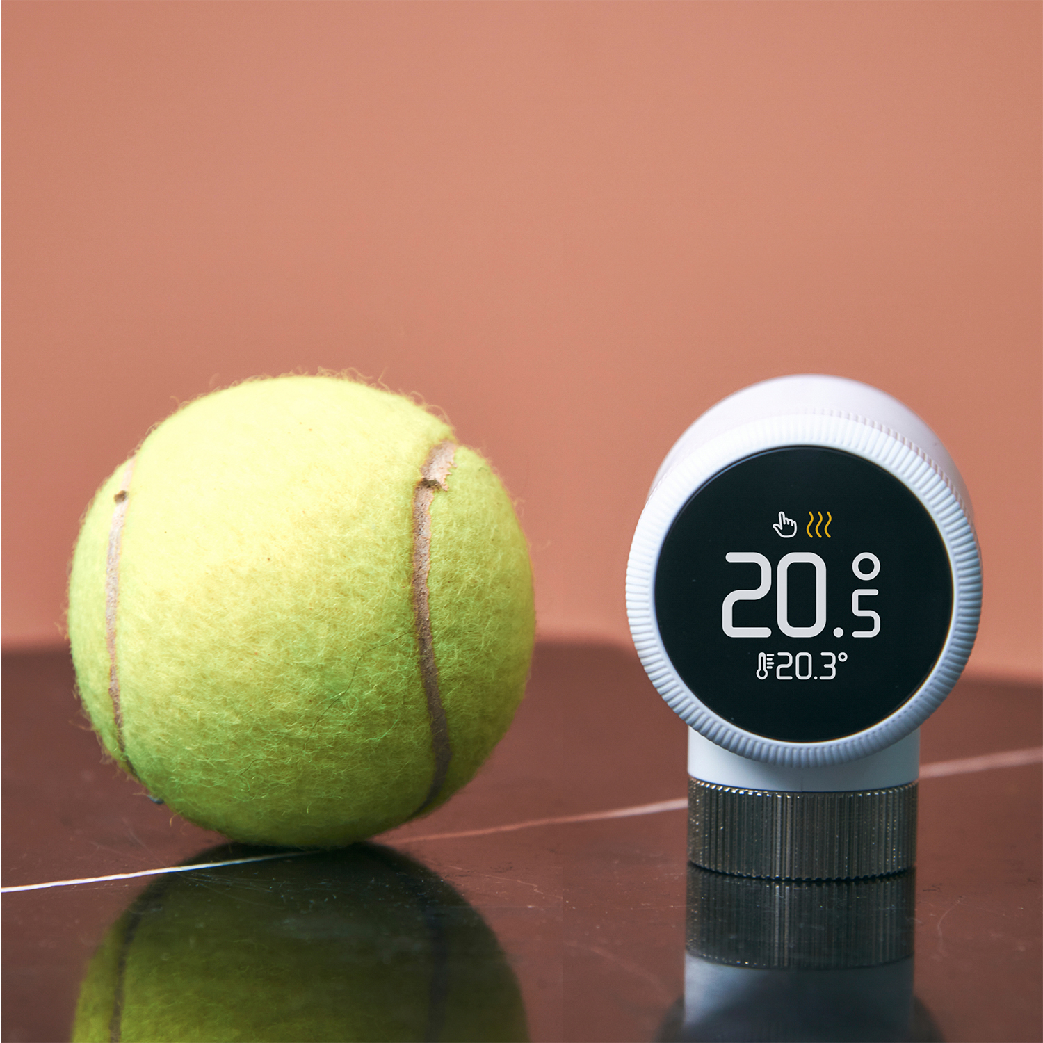 Palla da tennis e termostato. Il termostato mostra 20,5°C, 20,3°C. Bianco e nero.