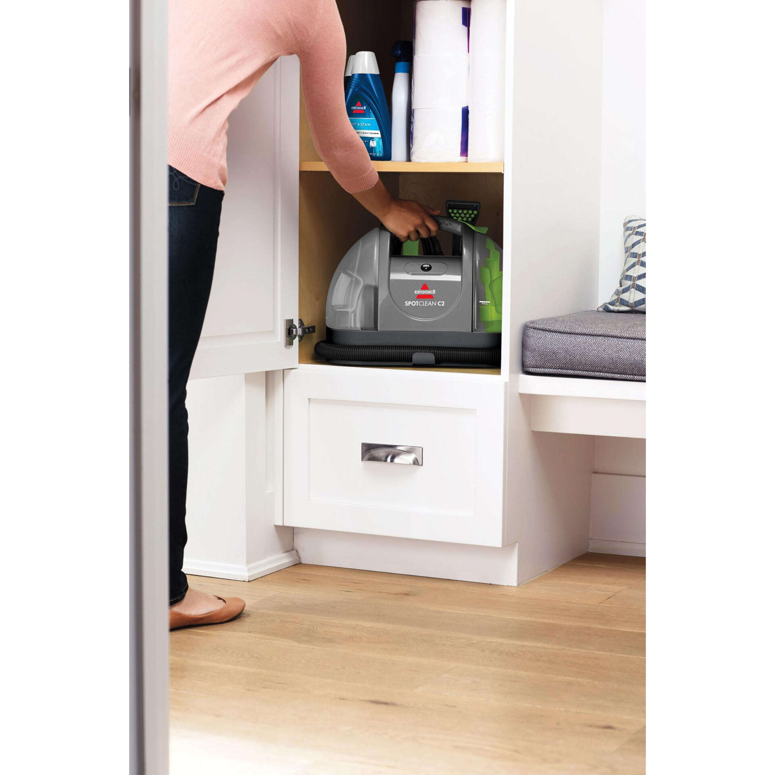 Frau öffnet Schrank mit grauem Bissell SpotClean C3 Reiniger; Holzfußboden.