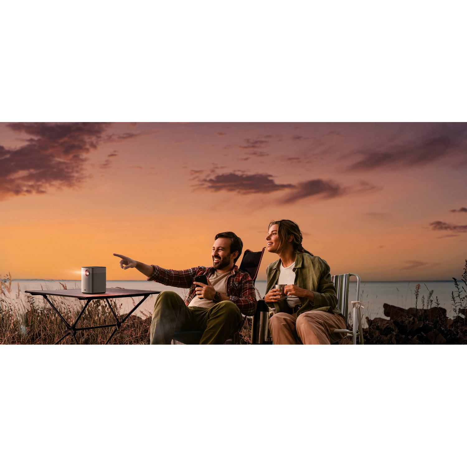Deux personnes sont assises et regardent un projecteur. Le ciel est orange au coucher du soleil.