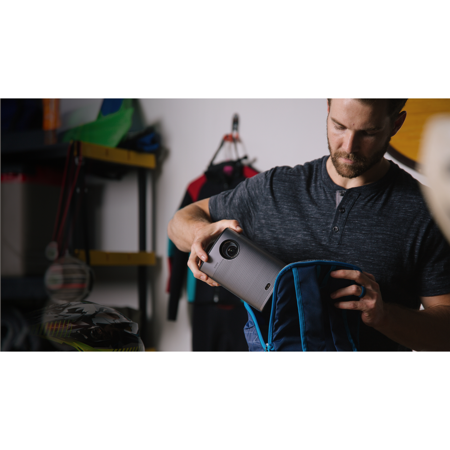 Un homme range un appareil gris dans un sac à dos bleu. Garage en arrière-plan.