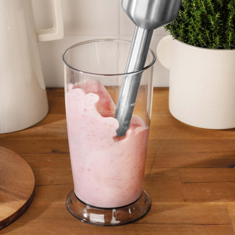 Mixer in einem Glas mit rosa Flüssigkeit und einem Holzbrett.