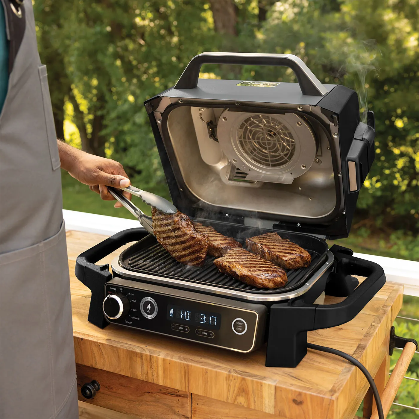 Személy steak-et süt egy nyitott, fekete grillen digitális kijelzővel és fogantyúval.