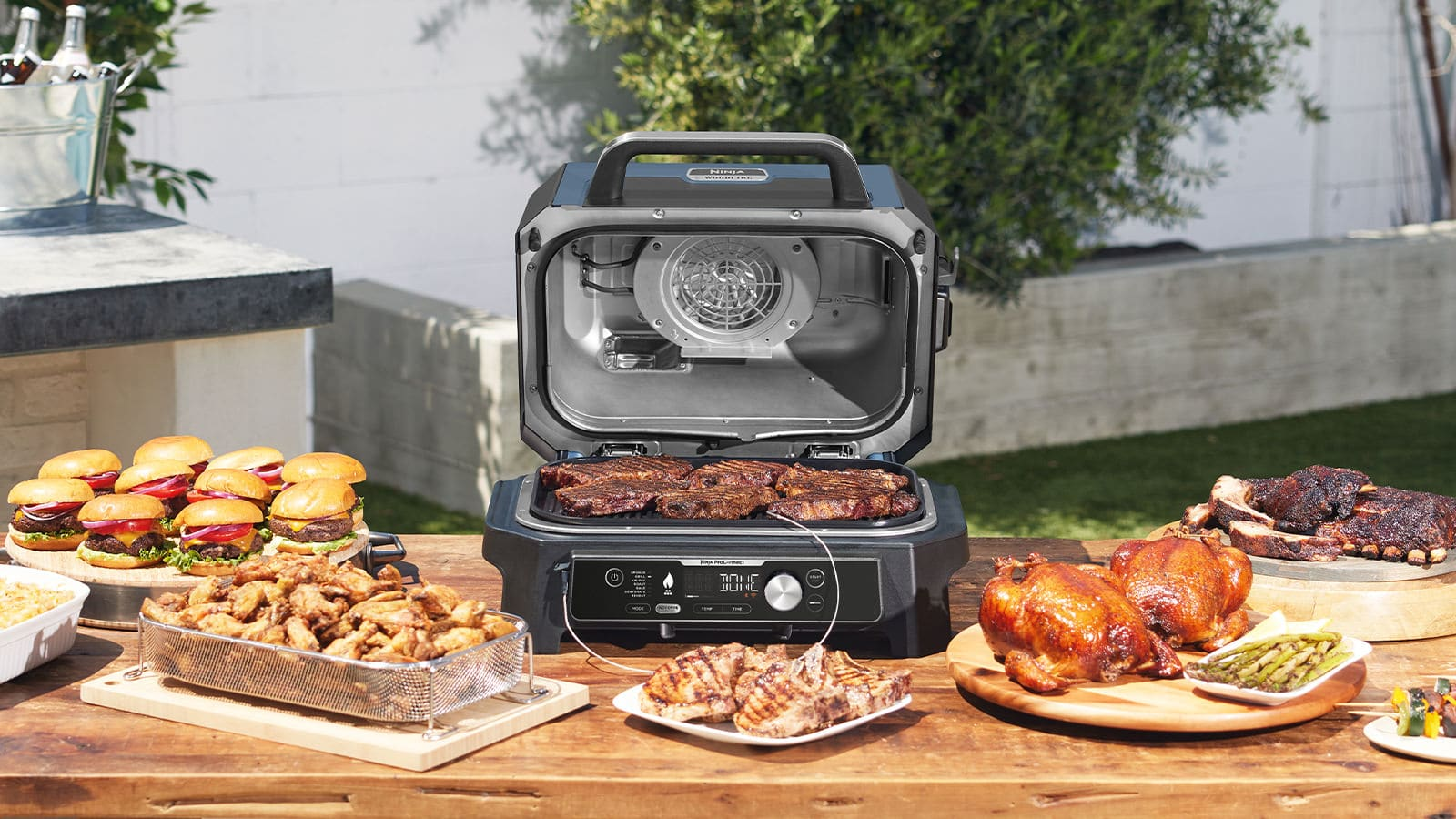 Kültéri grill sült ételekkel egy faasztalon. Hamburgerek, csirke és bordák láthatók.