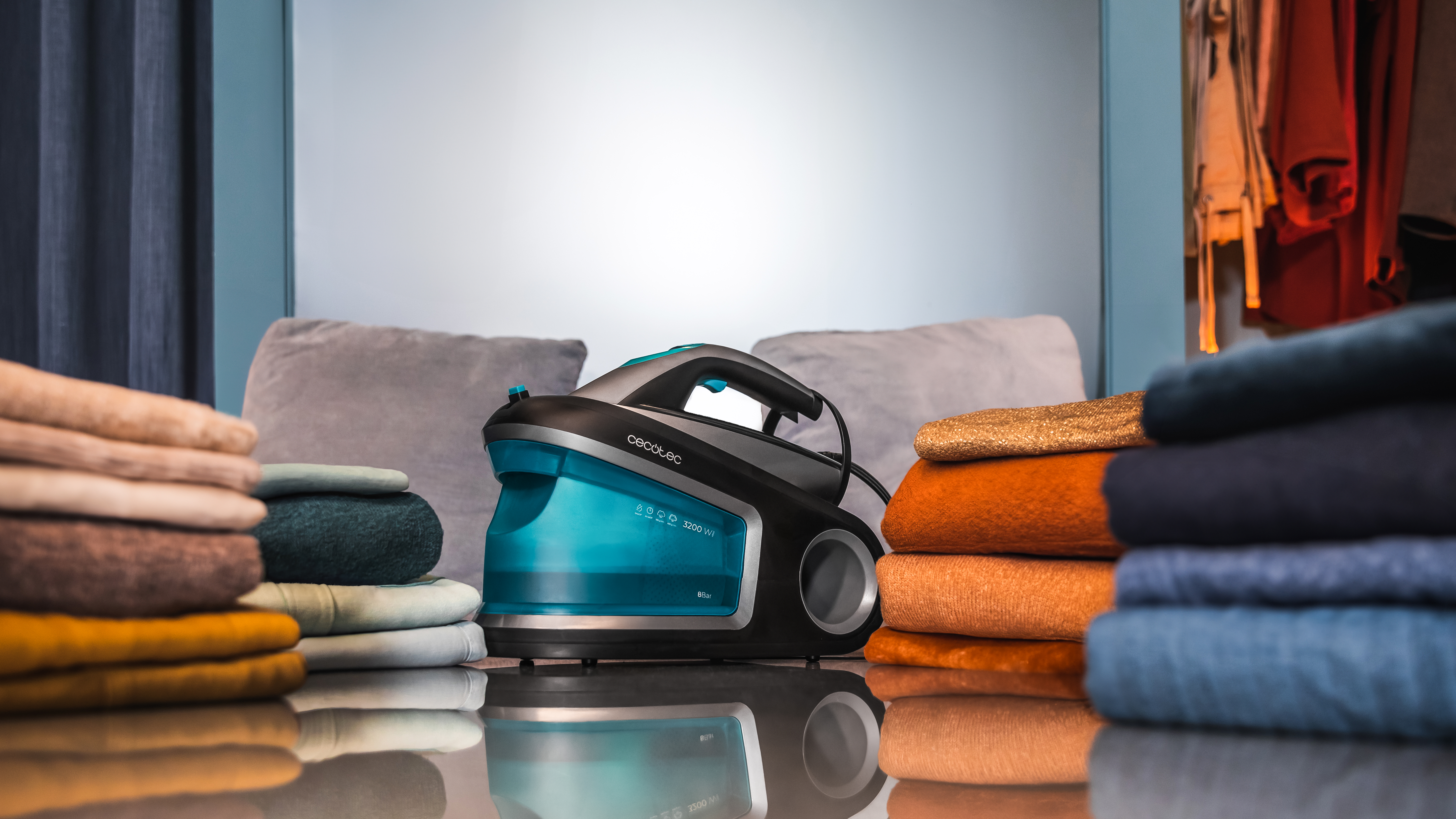 Limpiador a vapor sobre una mesa con ropa doblada y almohadas. Azul y negro.