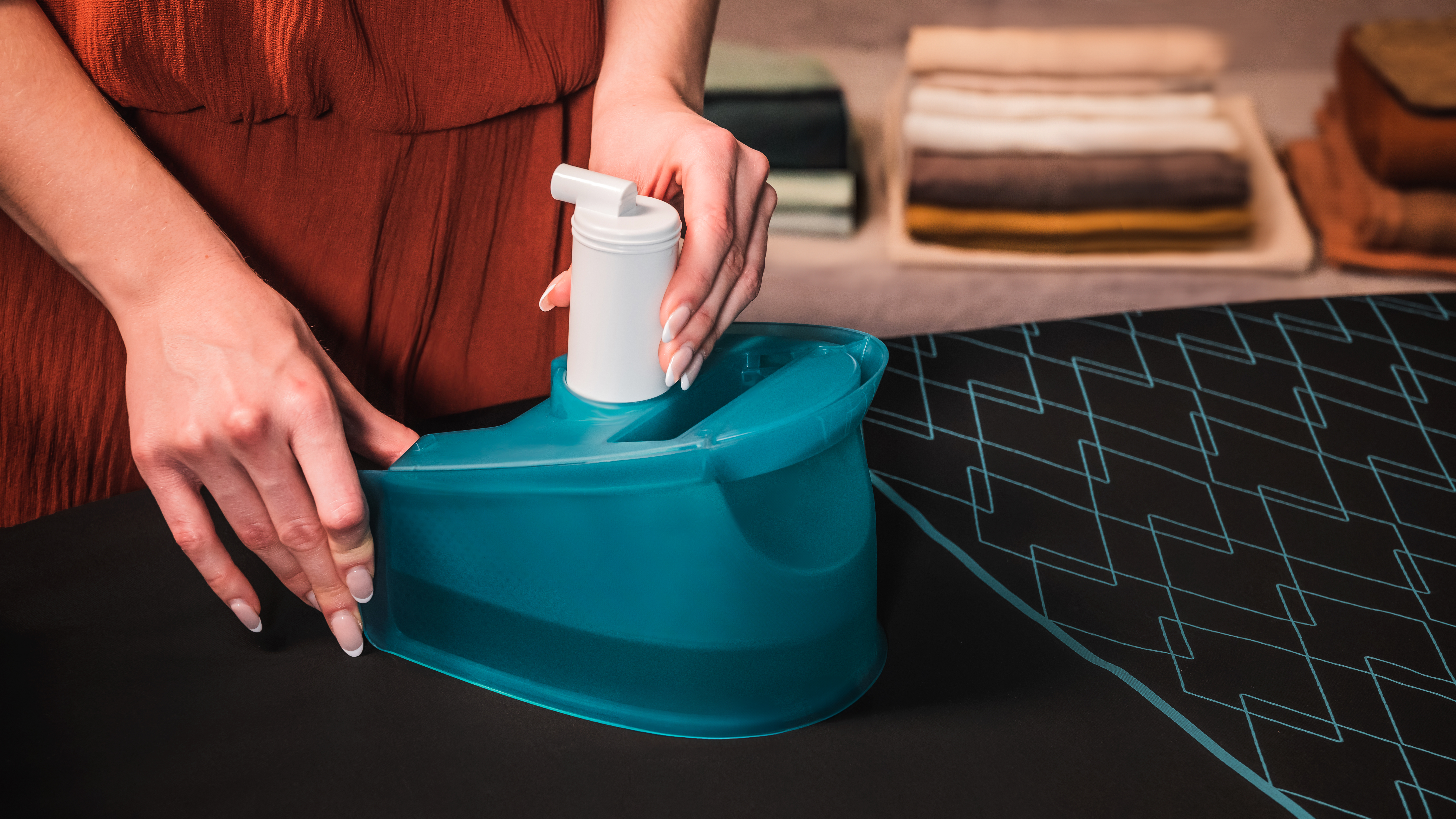 Persona llenando un recipiente de agua para una plancha, con una tabla de planchar azul de fondo.