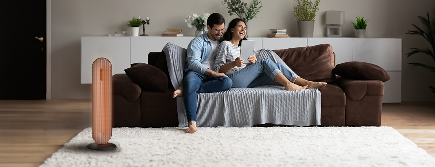 Pareja en un sofá, sonriendo, mirando una tableta. Un calefactor está cerca.
