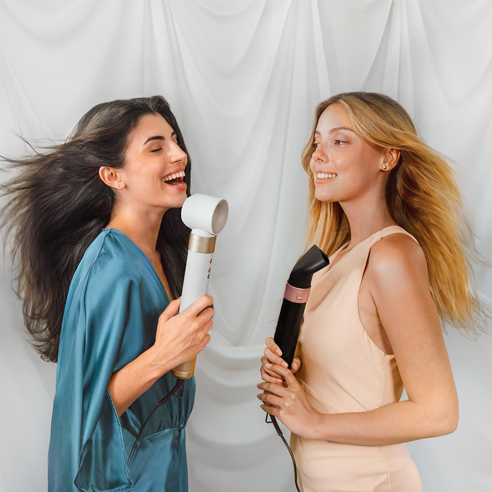 Dos mujeres cantando en secadores de pelo, una con cabello oscuro, otra con cabello rubio.