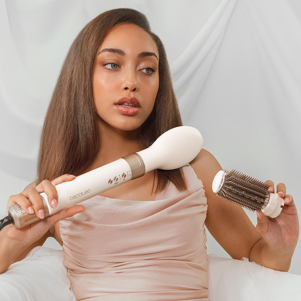 Una mujer sosteniendo un dispositivo para peinar el cabello con un accesorio de cepillo, mirando fuera de cámara.