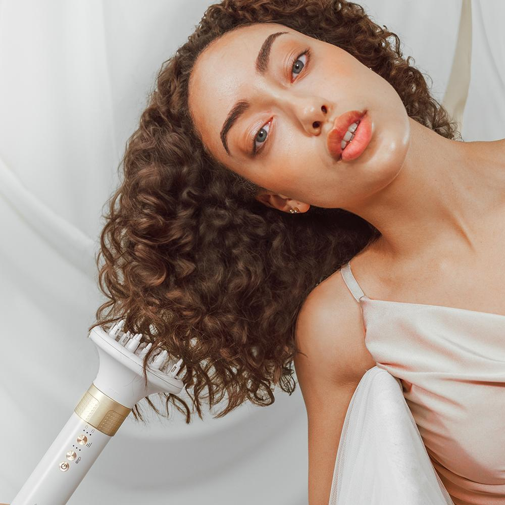 Mujer con cabello rizado secándolo con un secador de pelo blanco y dorado.