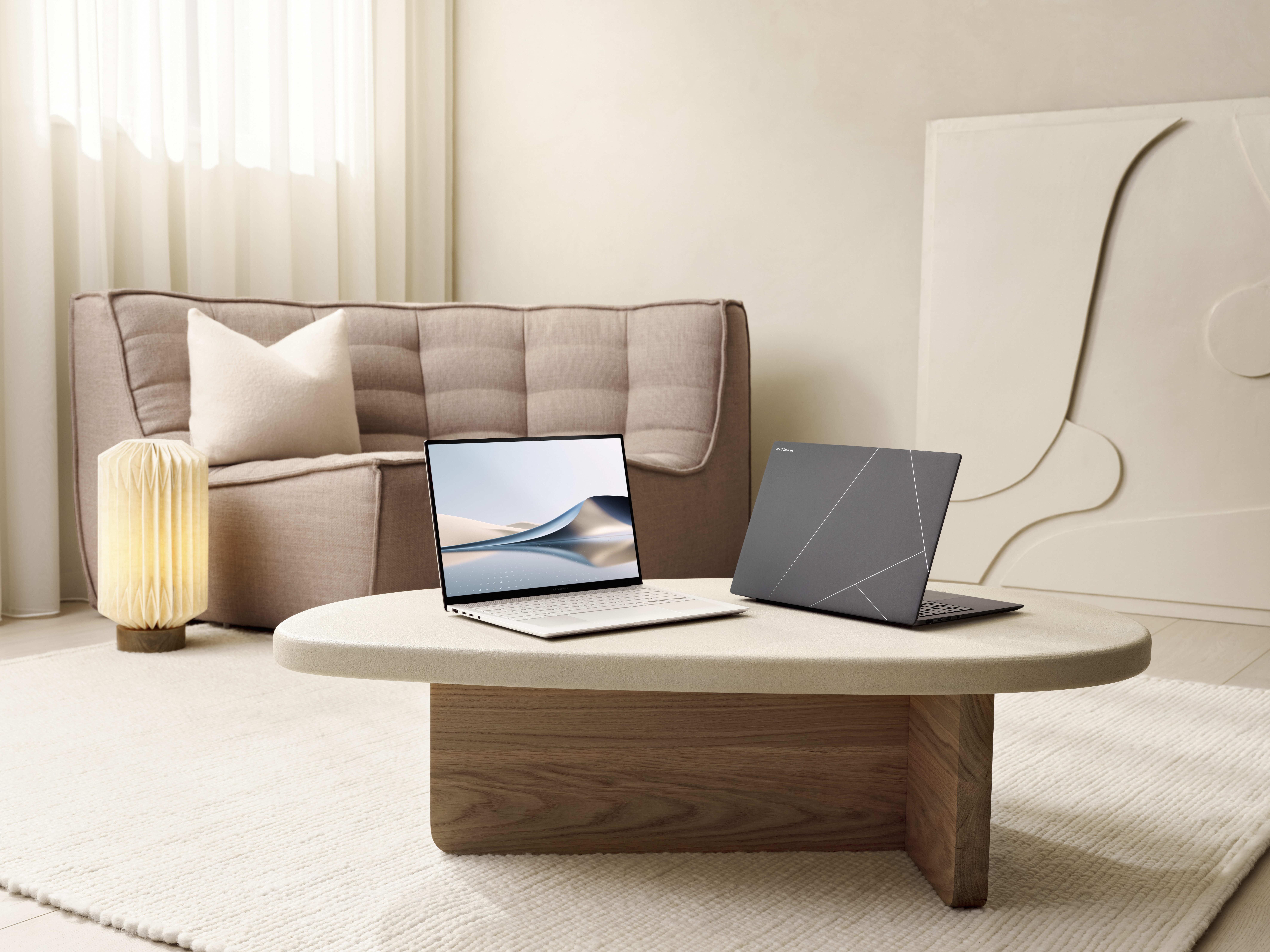 Zwei Laptops auf einem Tisch. Einer offen, der andere geschlossen. Ein beiges Sofa und eine Lampe sind im Hintergrund.