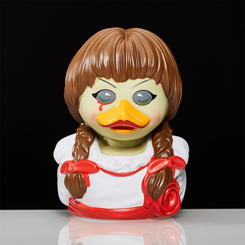 Egy kacsaszerű baba Annabelle arcával, fehér felületen ül.