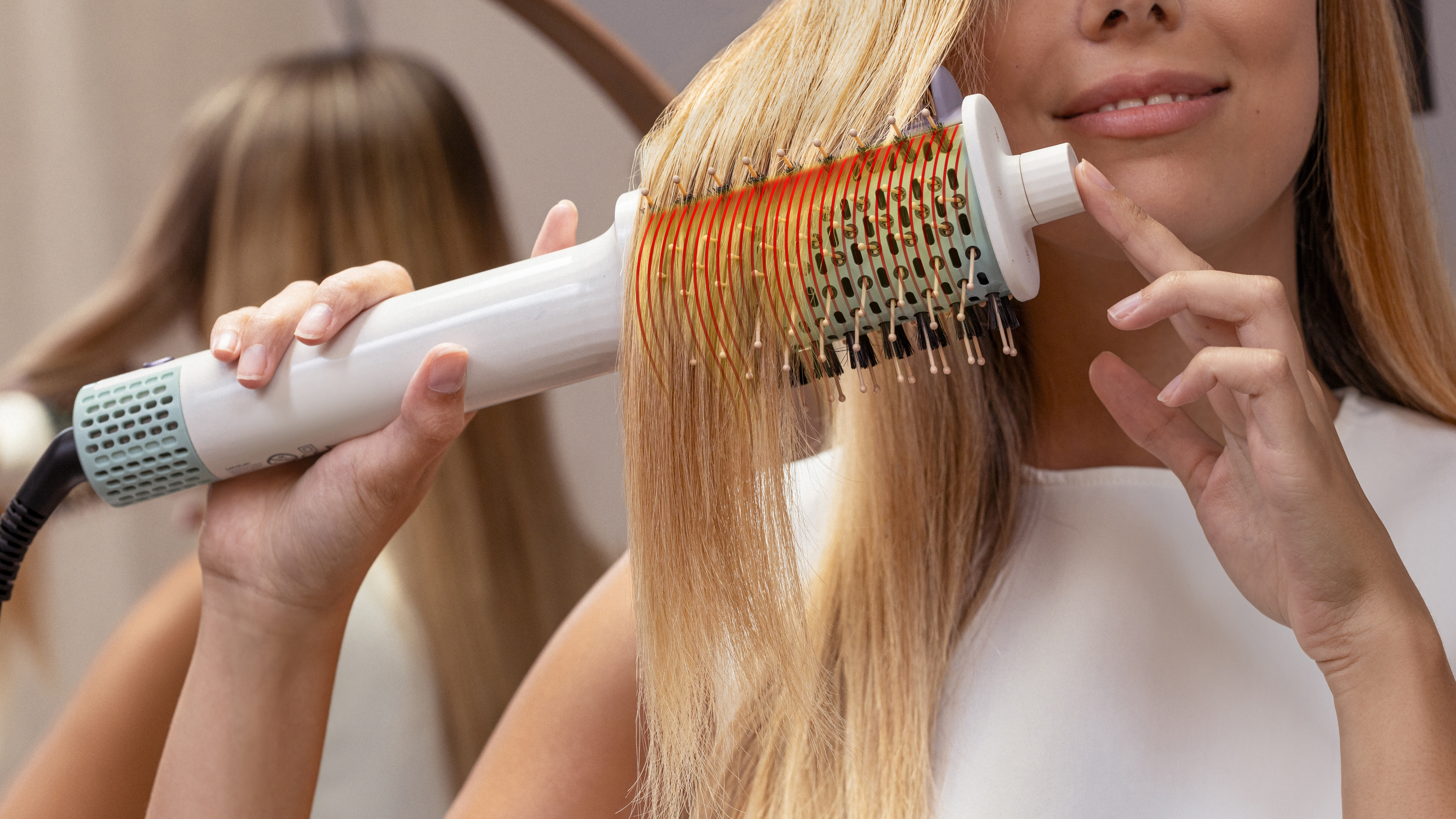 Una persona peinando su cabello mojado con un cepillo redondo, con reflejo en el espejo.