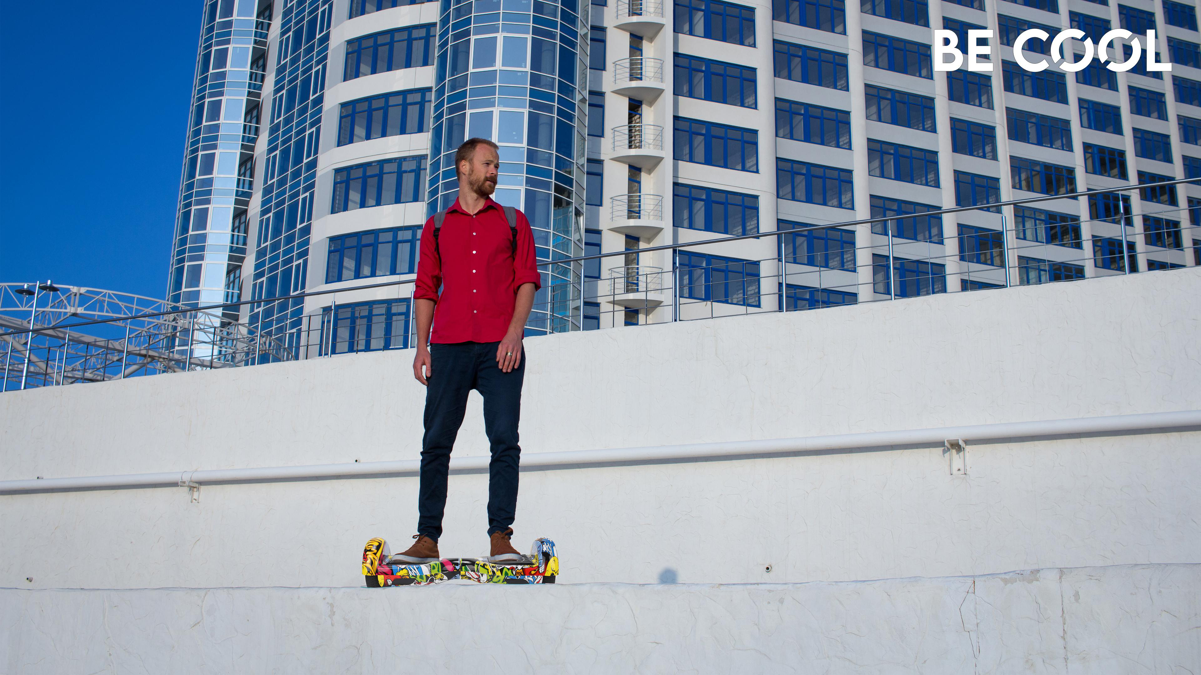Mann fährt Hoverboard auf einer Mauer, Gebäude im Hintergrund.
