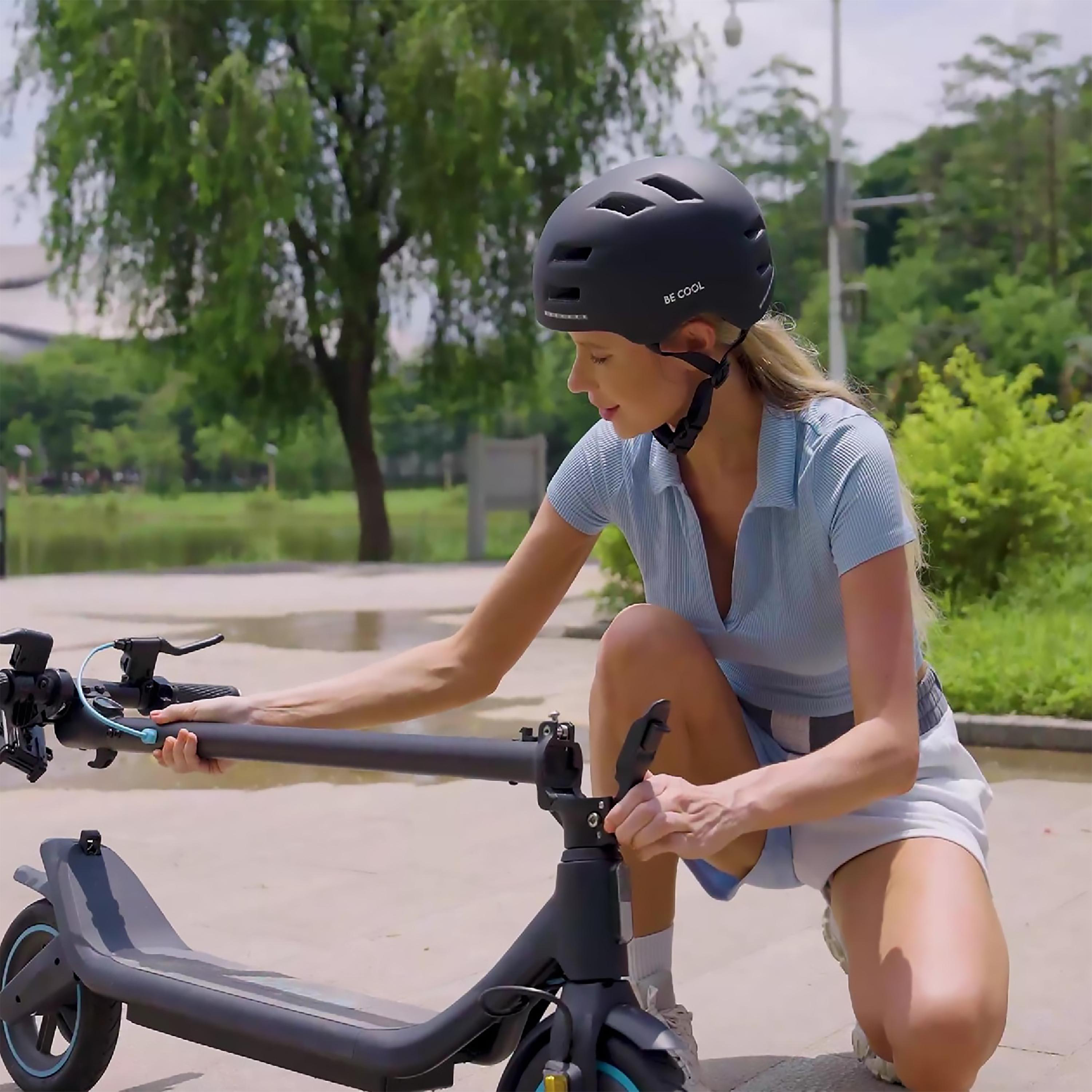 Eine Frau kniet, um einen Elektroroller einzustellen, mit Helm. Hintergrund: Park.