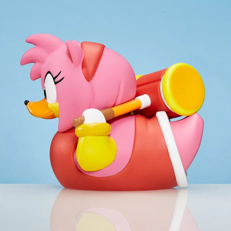 Amy Rose gumikacsa játék kalapácsot tart. Kék háttér, oldalnézet.