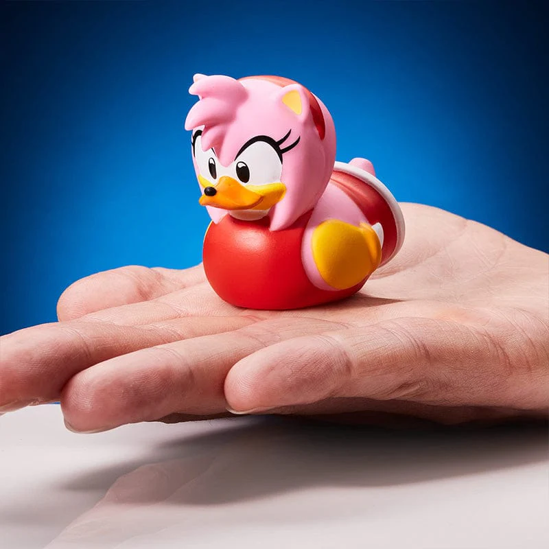 Amy Rose gumikacsa kézben, kék háttérrel.