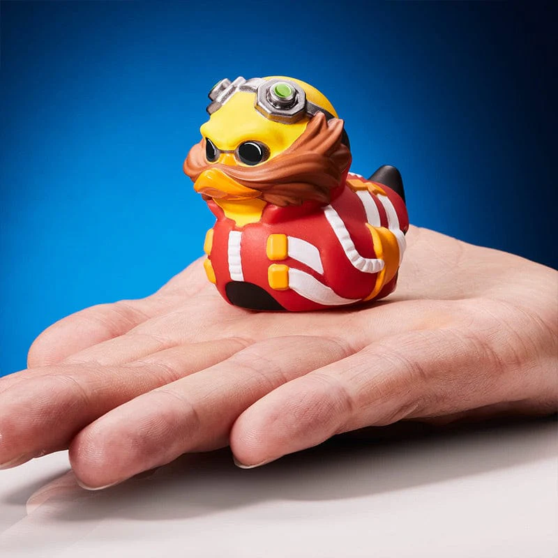 Sárga gumikacsa Dr. Eggman-nek öltözve. A kacsa egy kézen van. Kék háttér.