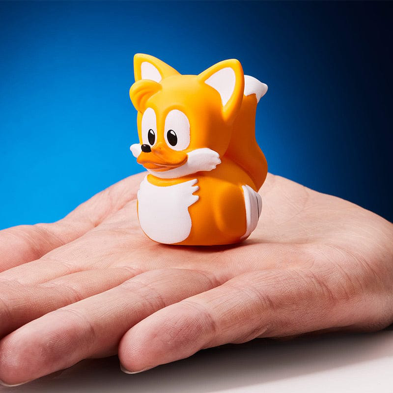 A Tails the fox gumikacsa egy kézen nyugszik kék háttér előtt.