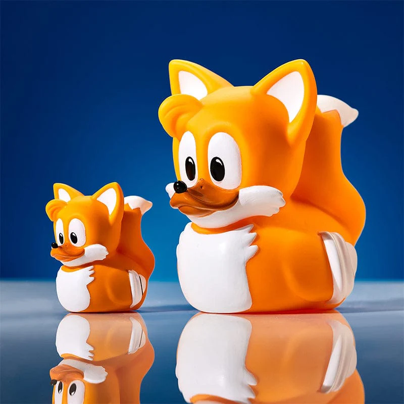 Két narancssárga Tails kacsa játék, egy nagy, egy kicsi, kék felületen, tükröződésekkel.